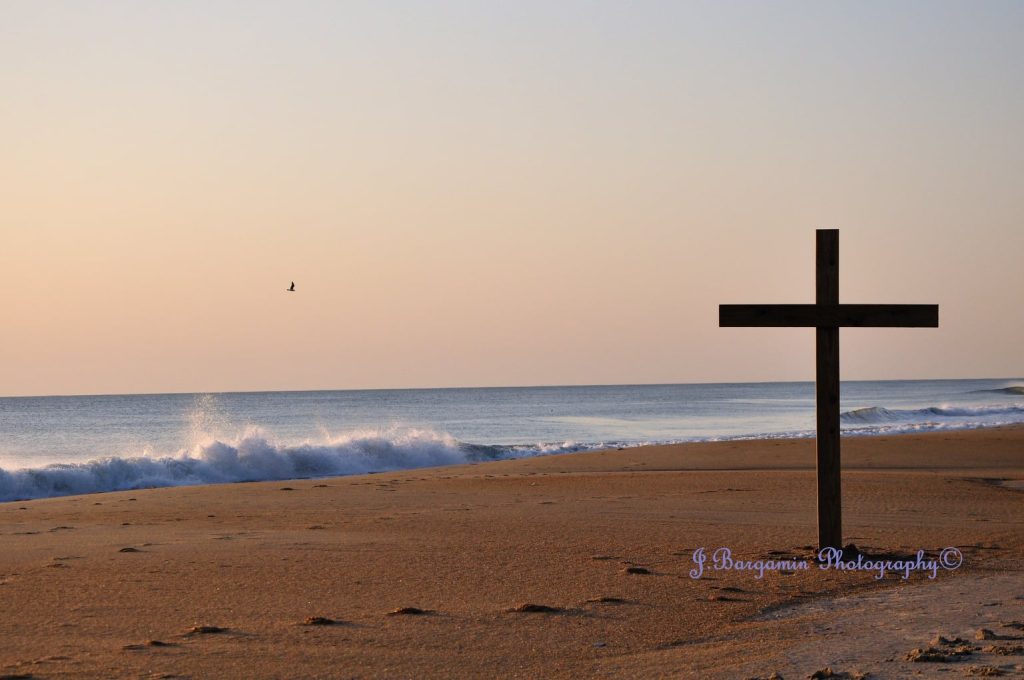 Simple wooden Cross at the shoreline on the beach on a beautiful calm early Easter morning.