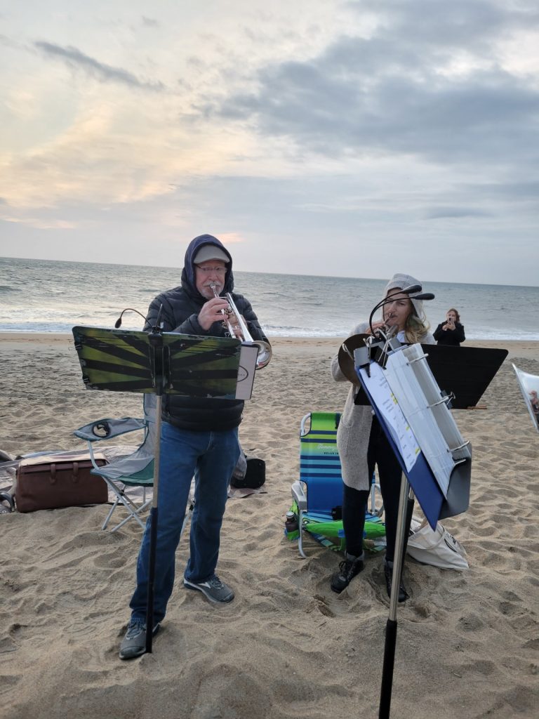 Early cold morning at the beach. Two musicians are playing brass instruments. The man in the hat and jacket is playing a trumpet and the young lady is playing a french horn.