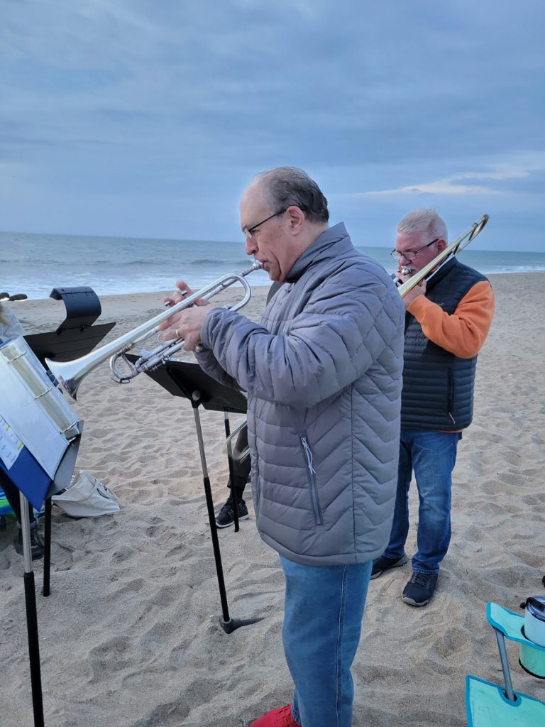 Early cold morning at the ocean. Two men are playing brass instruments. The man in the gray coat is playing a trumpet and the man behind him is playing a trombone